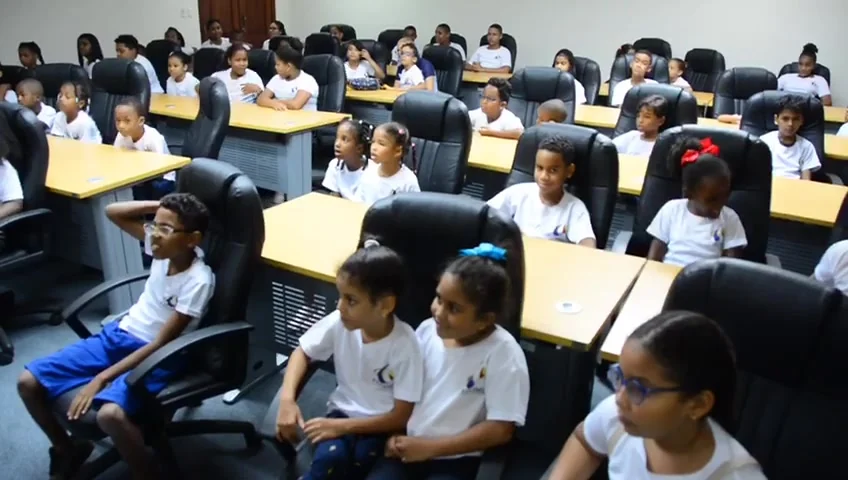 Niños y niñas del campamento de hijos de empleados de Fedomu sentados en la sala de reuniones de la institución