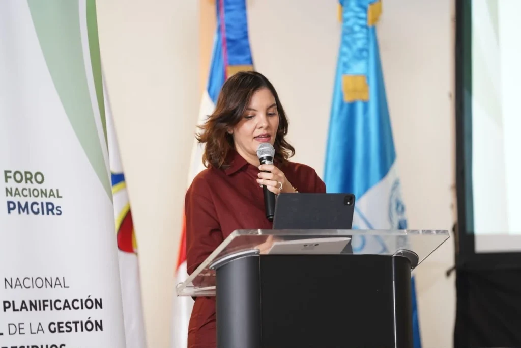 Ana Emilia Pimentel habla al micrófono en el atril, con una tableta delante y las banderas al fondo