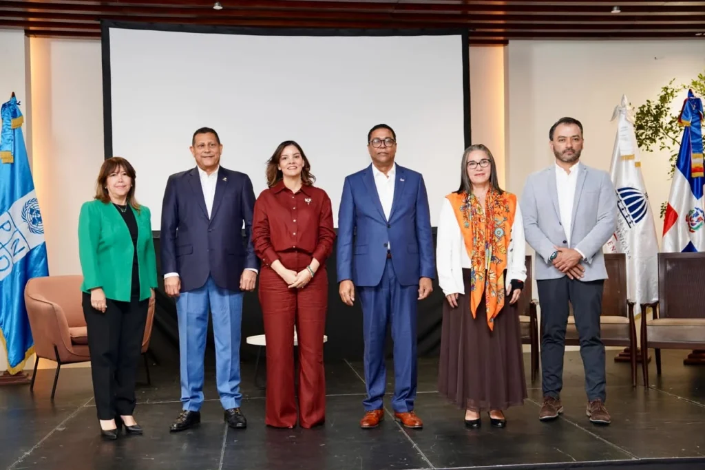 Seis autoridades de pie en la tarima del foro, ante la pantalla y las banderas de la República Dominicana y del PNUD