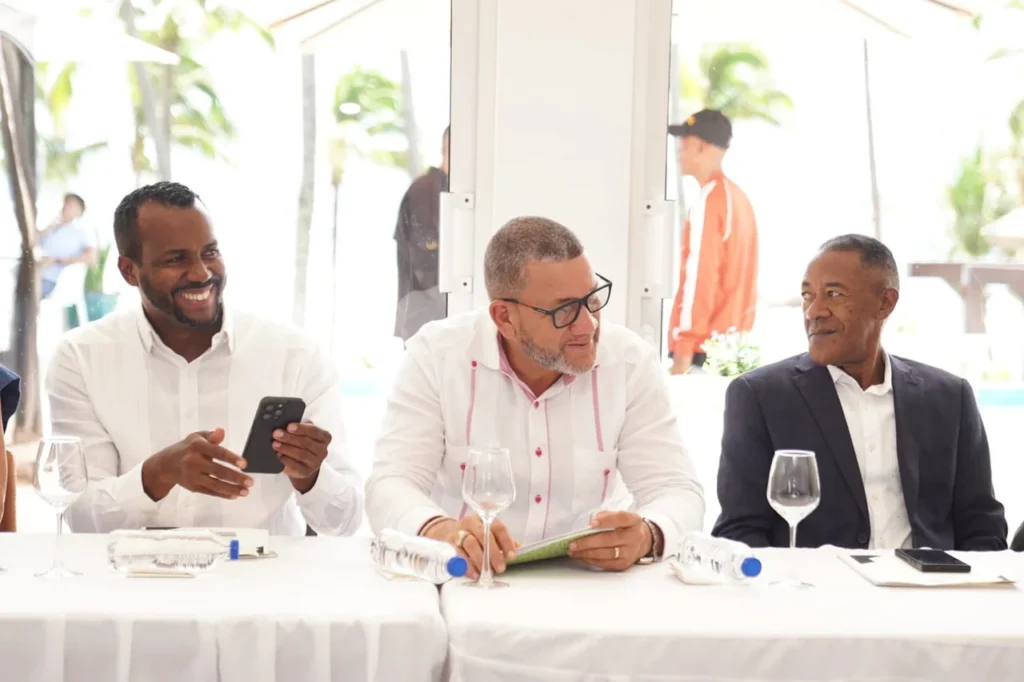 Tres alcaldes sentados a la mesa durante la asamblea; uno de ellos toma una foto con su teléfono