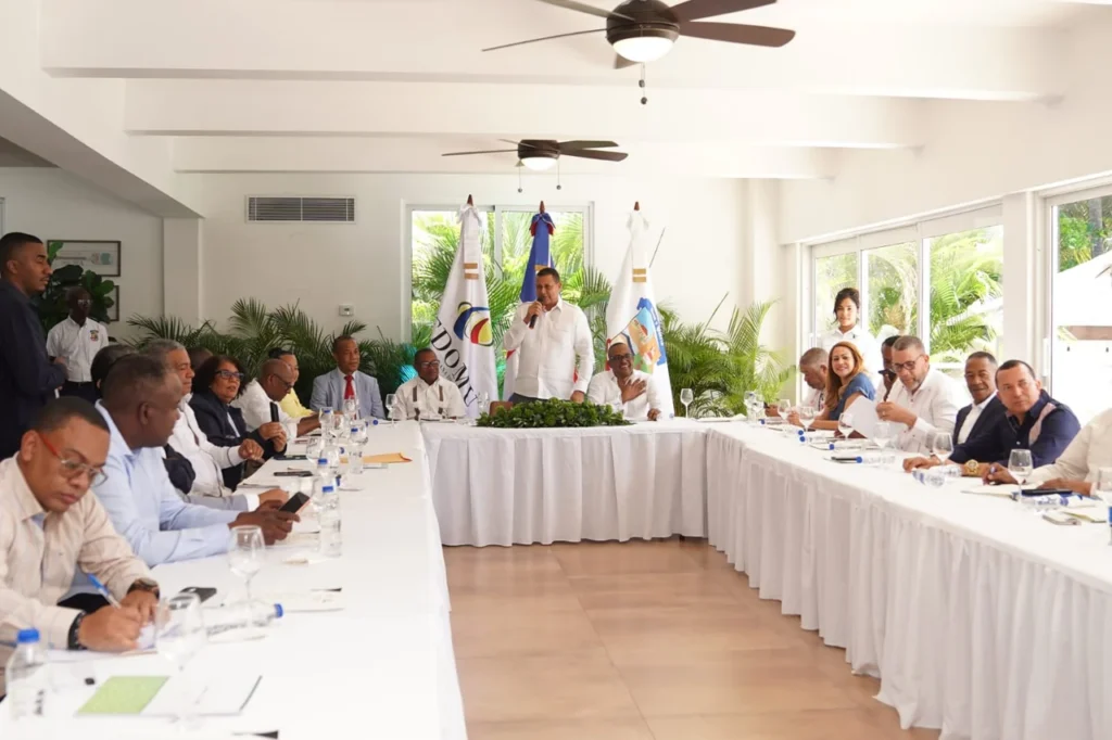Vista general del salón: Nelson Núñez, de pie, se dirige a los alcaldes sentados en mesas en U durante la Asamblea de Fedomu Región Valdesia