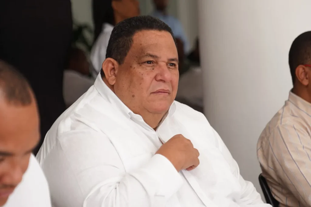 Rafael Antonio Hidalgo Fernández, alcalde de Azua, sentado con camisa blanca, escucha con la mano en el pecho