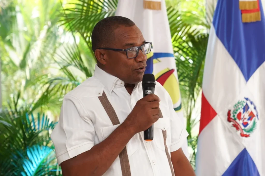 Víctor Figuereo, alcalde de Pueblo Viejo, habla al micrófono de pie junto a la bandera dominicana