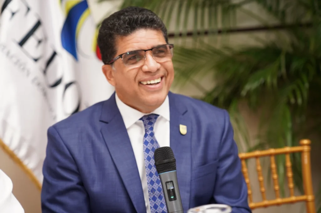 Dio Astacio sonríe con un micrófono frente a la bandera de Fedomu