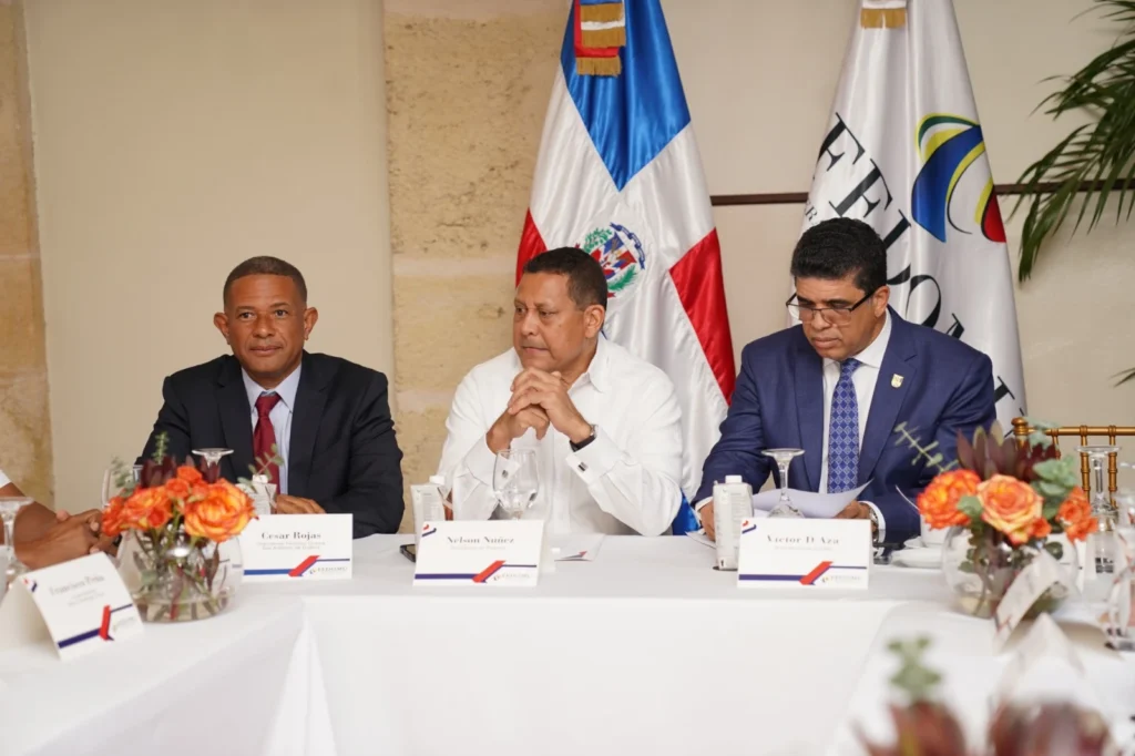 César Rojas, Nelson Núñez y Dio Astacio sentados en la mesa principal con las banderas detrás