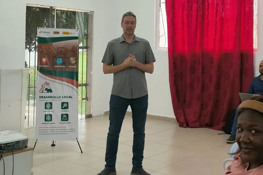 Alberto García habla de pie en el salón, junto al pendón del proyecto Desarrollo Local