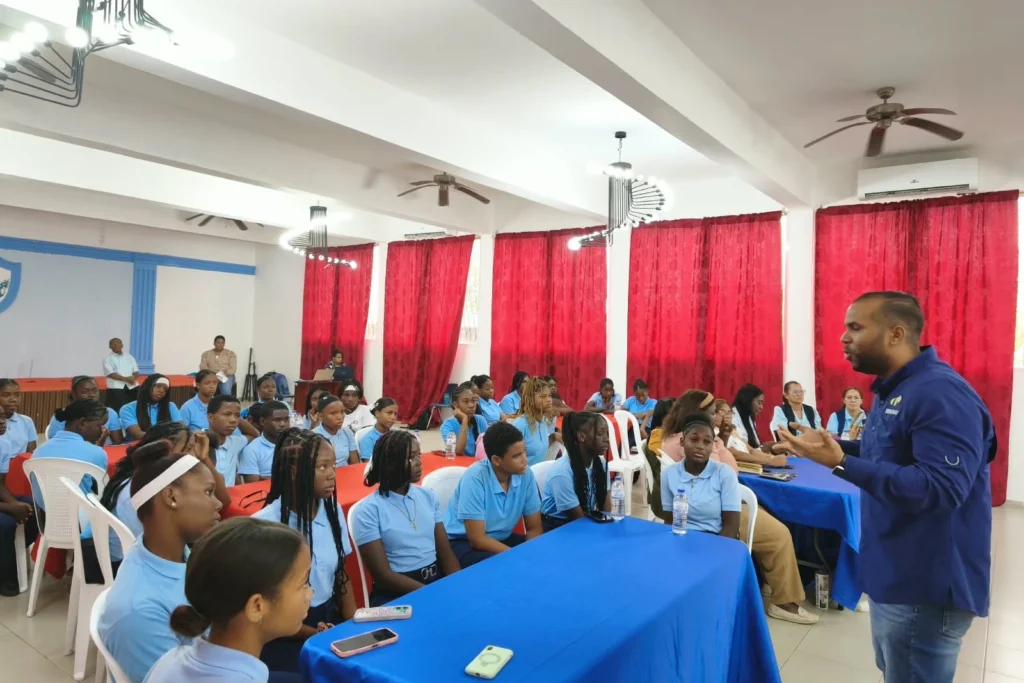Bienvenido Jiménez, con camisa de Fedomu, se dirige a los estudiantes sentados a mesas con manteles azules y rojos