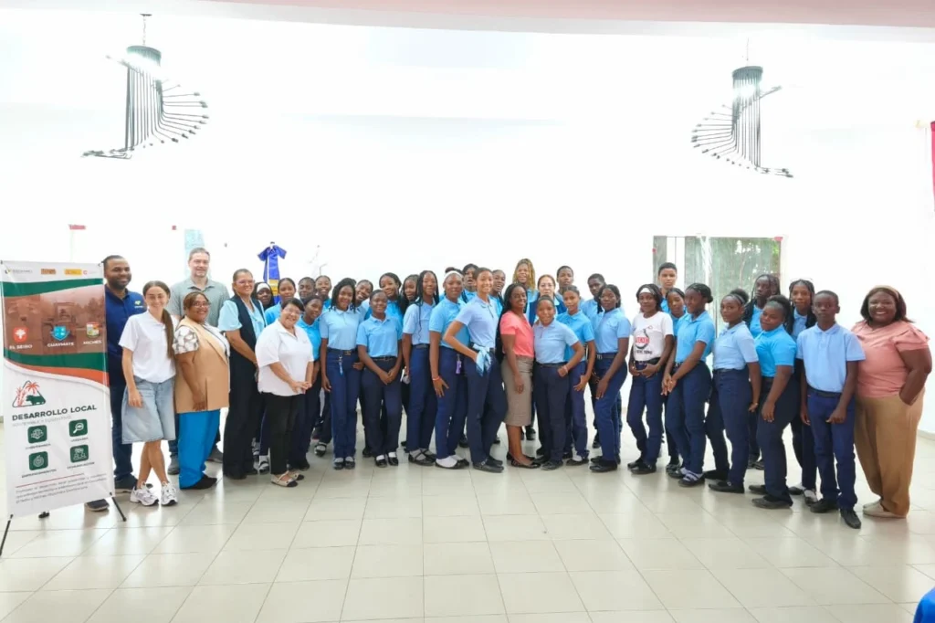Grupo de estudiantes con uniforme azul claro posa con docentes y el equipo del proyecto junto al pendón Desarrollo Local de El Seibo, Guaymate y Miches