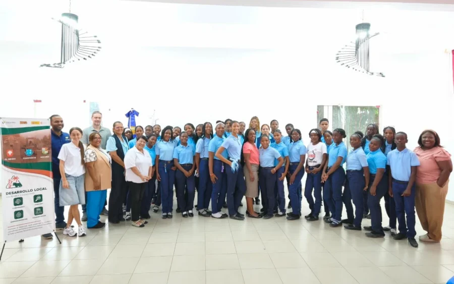 Grupo de estudiantes con uniforme azul claro posa con docentes y el equipo del proyecto junto al pendón Desarrollo Local de El Seibo, Guaymate y Miches